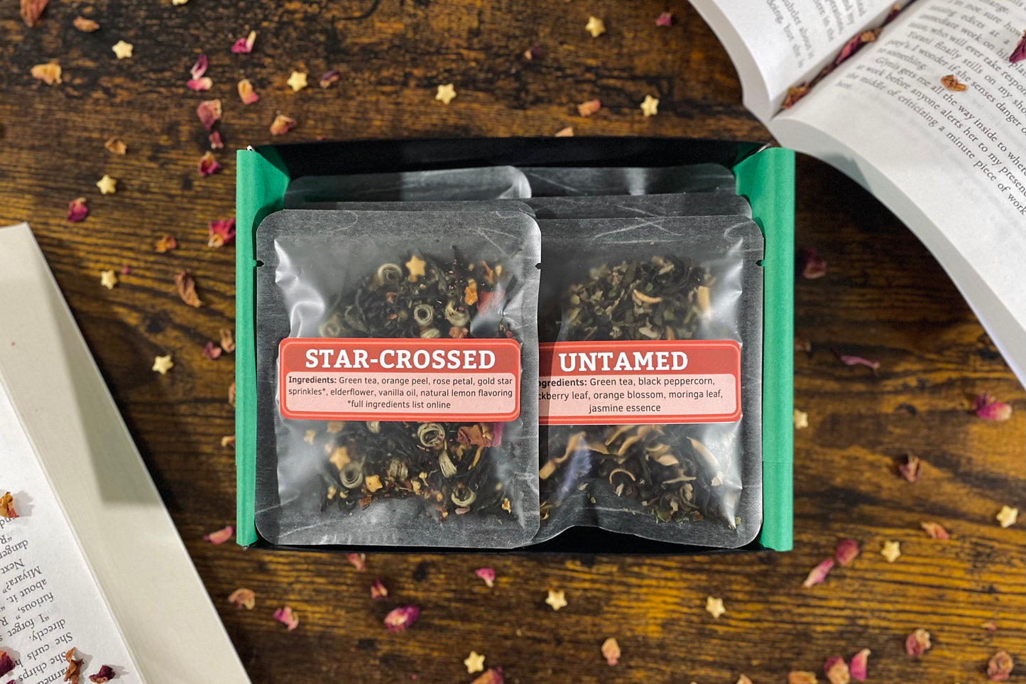 Two tea packages labeled 'Star-Crossed' and 'Untamed' on a wooden surface with flowers.