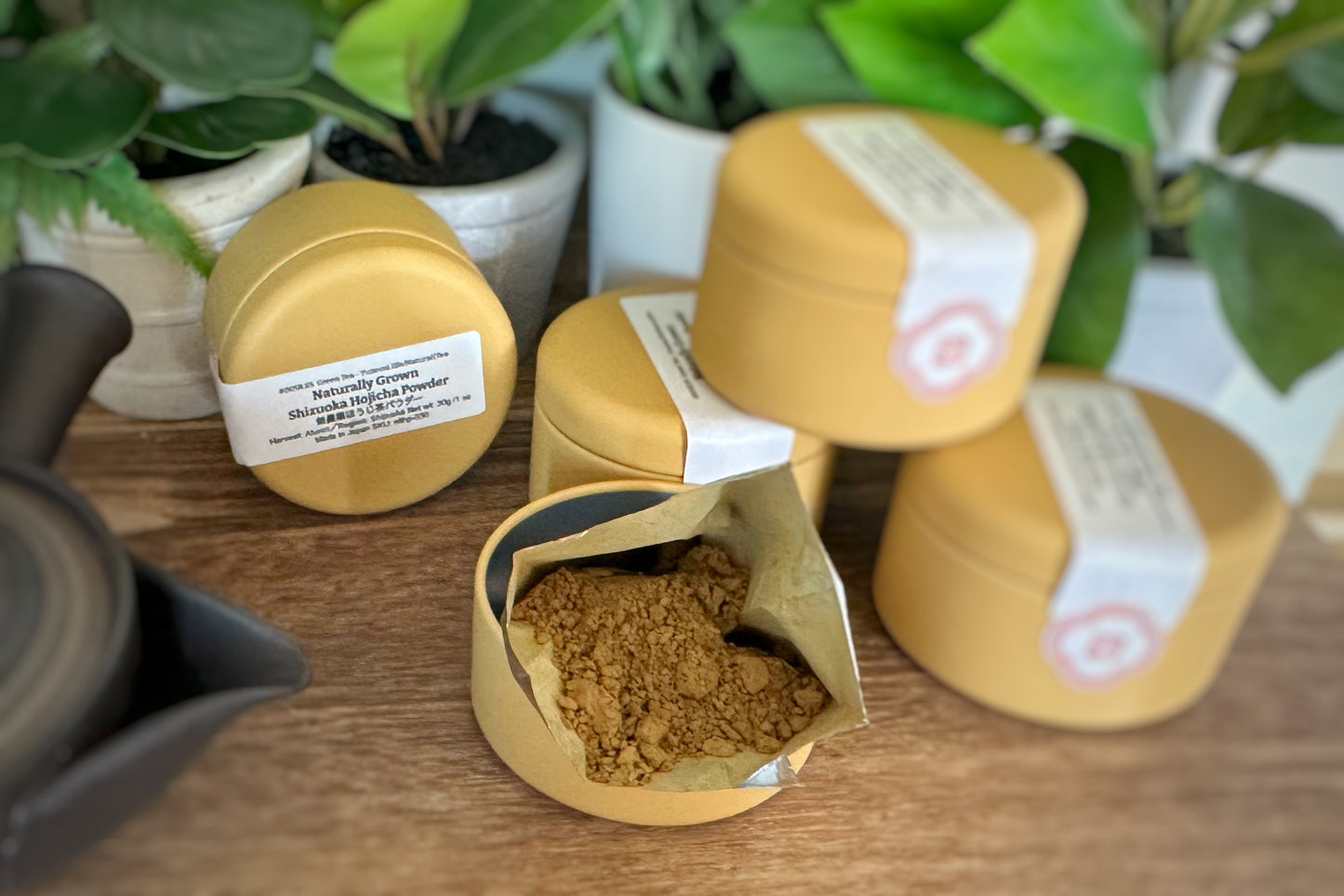 Gold containers with tea powder on a wooden surface with plants in the background