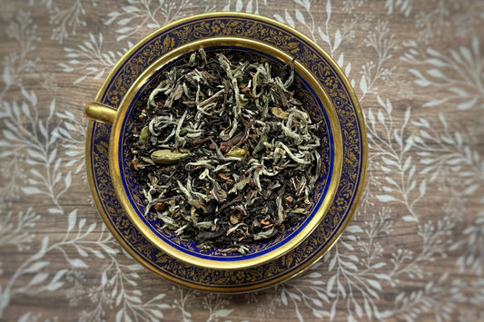 Dry tea leaves in a decorative blue and gold bowl on a wooden surface with leaf pattern