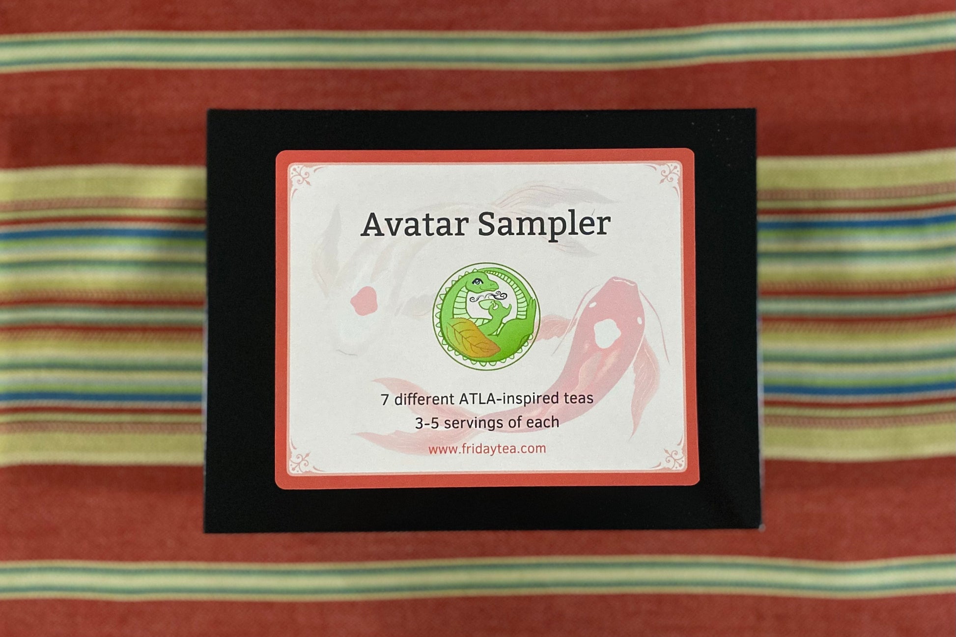 A closed black sample box with Avatar-themed label design on a colorful cloth