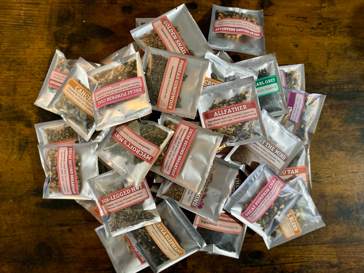 A pile of small silver-backed windowed pouches containing loose herbal tea samples
