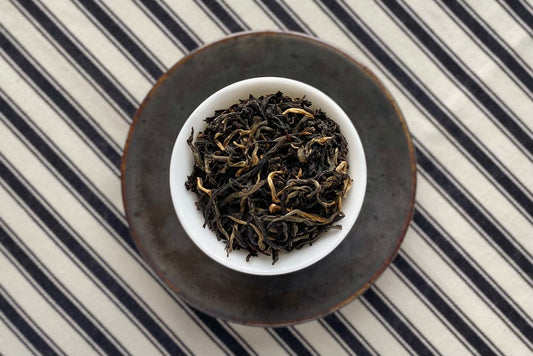 Teacup full of black tea with some gold tips